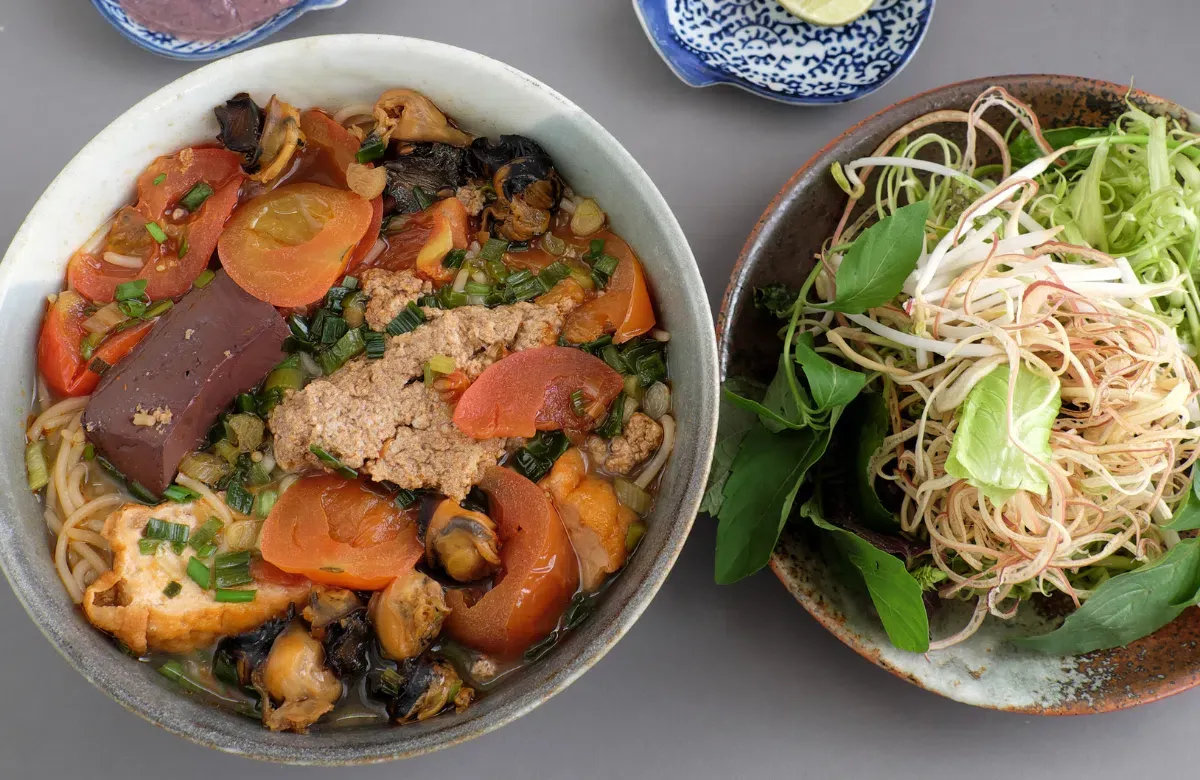 Một tô bún riêu cua đầy đủ với riêu cua, đậu phụ, huyết và các loại rau sống ăn kèm