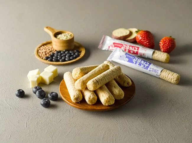 Em bé 6 tháng tuổi đang tập cầm bánh ăn dặm hình que với bàn tay nhỏ xinh