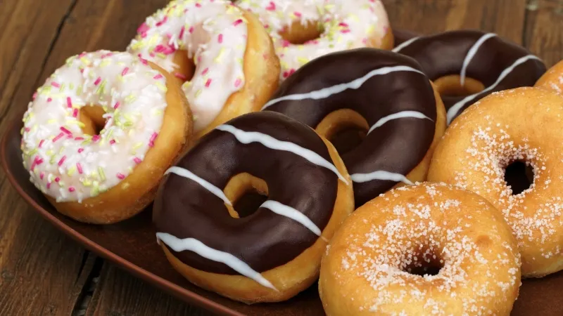 Ba chiếc bánh donut với các loại lớp phủ khác nhau, bao gồm sô cô la hạt, đường trắng và dừa nạo, được sắp xếp trên một chiếc đĩa trắng.