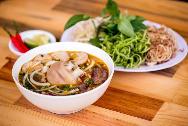 Một tô bún bò Huế đầy đặn với thịt bò, chả, tiết và các loại rau thơm tươi ngon