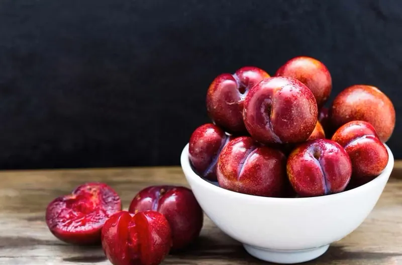 Một đĩa mận Bắc tươi ngon, được xếp gọn gàng, bên cạnh một rổ mận lớn khác