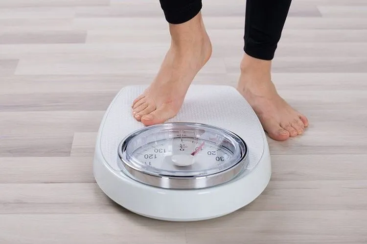 Một người đang cân trọng lượng cơ thể, minh họa vai trò của cân nặng trong việc tính toán lượng calo tiêu thụ khi đi bộ