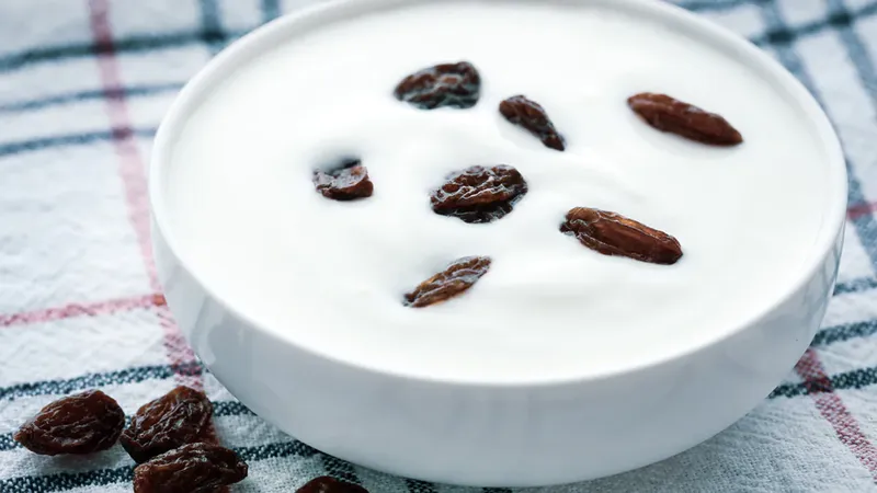 Hộp sữa chua trắng kết hợp với nho khô, tạo nên món ăn vặt bổ dưỡng và hỗ trợ tiêu hóa, phù hợp cho người ăn kiêng