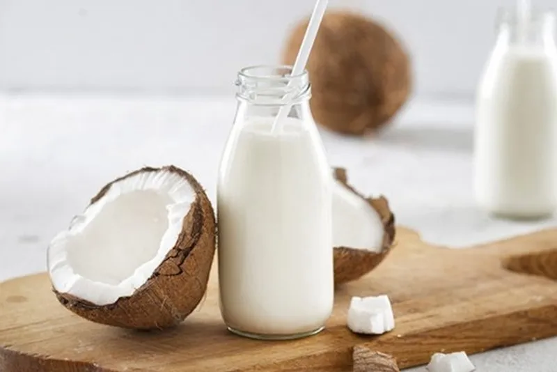 Một phụ nữ đang dùng muỗng múc nước cốt dừa vào ly smoothie, thể hiện sự tăng cường miễn dịch từ thực phẩm