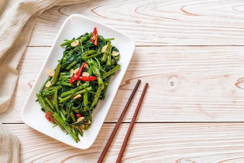 Người phụ nữ đang lựa chọn rau muống tươi tại chợ, chú trọng an toàn thực phẩm