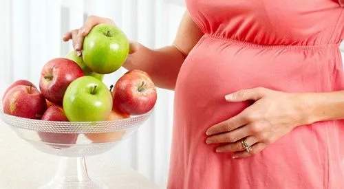 Người phụ nữ mang thai vui vẻ cầm quả táo trên tay