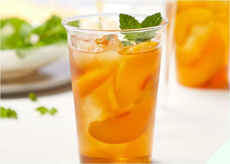 Một cốc trà đào đặt trên bàn với trái đào tươi và hoa đào, tượng trưng cho mùa xuân và sự tươi mới